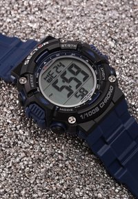 Orologio digitale con cinturino in silicone blu e cassa in plastica nera. Presenta un ampio display LCD che mostra l'ora, la data e altre funzioni.
