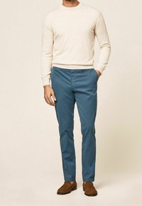 Light beige crew-neck sweater, blue slim-fit trousers, and brown loafers. The outfit features a relaxed design and smooth textures.