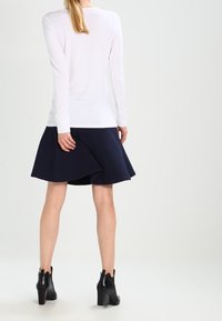 Camicia bianca a maniche lunghe abbinata a una gonna a campana blu scuro. La gonna presenta un motivo testurizzato ed è abbinata a stivaletti neri alla caviglia.