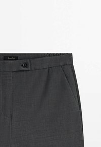 Pantalon gris foncé sur mesure avec fermeture à boutons sur le devant, poches latérales et bande élastique à la taille, posé à plat sur une surface blanche.