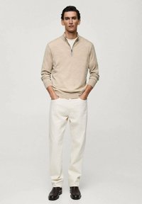 Beige sweater with a quarter-zip collar, white shirt underneath, paired with white trousers and dark brown boots. Smooth texture.