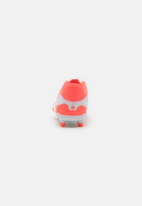 Crampon de soccer corail vif avec un dessus texturé, des accents blancs et six crampons sur la semelle pour une traction optimale. La vue arrière met en valeur un design élégant.