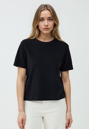 T-shirt noir en coton à manches courtes, col rond et embellissements texturés subtils. Coupé dans une coupe décontractée. Associé à un pantalon de couleur claire.