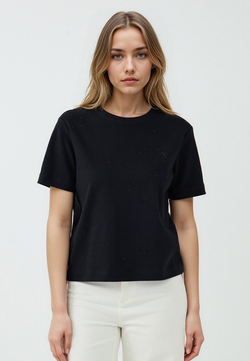 Zwarte katoenen t-shirt met korte mouwen, ronde hals en subtiele textuurelementen. Gemaakt in een relaxte pasvorm. Gepaard met lichte broek.