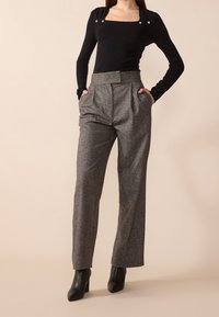 Czarny top z długim rękawem i kwadratowym dekoltem, zdobiony guzikami, w połączeniu z wysokim stanem szarymi spodniami w plisy i czarnymi botkami na obcasie.