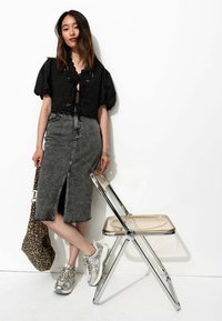 Blouse noire cropped à manches ballon, jupe en denim gris taille haute avec fente avant, baskets argentées, sac à imprimé léopard, chaise pliable transparente.