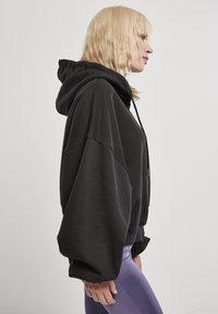 Felpa nera oversize con cappuccio, dal taglio rilassato, con maniche ampie e una texture morbida. Abbinata a leggings viola.
