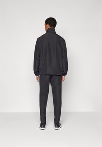 Μαύρο αθλητικό σακάκι με ψηλό γιακά, συνδυασμένο με παντελόνι που διαθέτει λευκές πλαϊνές ρίγες. Λείο, ματ ύφασμα, χαλαρή εφαρμογή.