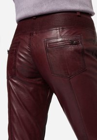 Burgunderfarbene Lederhosen mit glatter Textur, geripptem Taillenbund und zwei Gesäßtaschen mit Reißverschlüssen für zusätzliche Details.