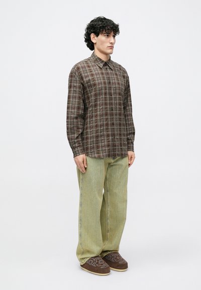 Brązowa koszula w kratę na guziki z jasnoniebieskimi akcentami, zestawiona z szerokimi jasnoniemowymi spodniami i brązowymi haftowanymi kapciami.