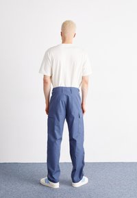 Blauwe cargobroek met een hoge taille, twee zijzakken en details van achterzakken, gecombineerd met een eenvoudige witte t-shirt en witte sneakers.