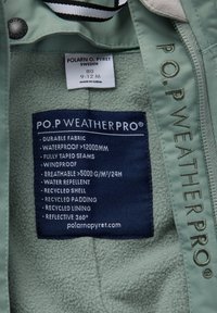 Kledinglabel op groene stof met details over Polarn O. Pyret WeatherPro functies: waterdicht, winddicht, ademend, gerecycled materiaal en reflecterend 360°.