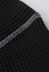 Schwarzer Strickstoff mit einer gerippten Textur und einem kontrastierenden weißen Stichdetail entlang der Naht, das die Qualität und das Design des Materials hervorhebt.