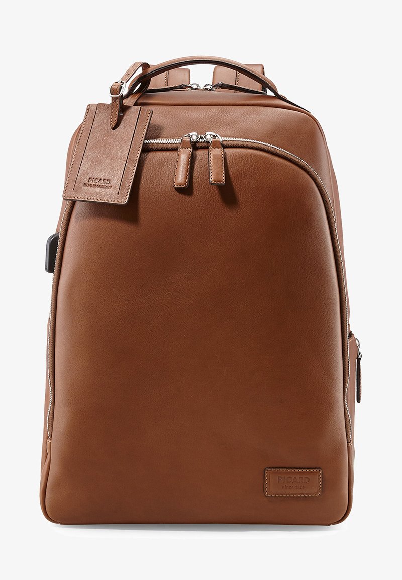Sac à dos en cuir brun avec une texture lisse, fermeture à double zip, étiquette avant et branding subtil. Il dispose de bretelles ajustables et d'un design épuré.