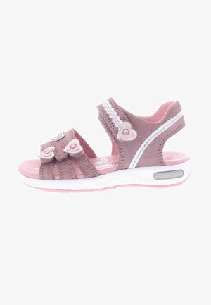 Różowy sandał dziecięcy z białą podeszwą, trzema regulowanymi paskami ozdobionymi sercowatymi dodatkami oraz miękką wyściółką pod stopą.