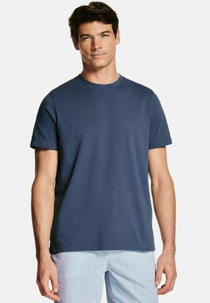 Homme portant un t-shirt uni bleu marine à manches courtes et un short rayé bleu clair, debout devant un fond blanc.