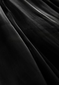 Un tissu noir et transparent drape élégamment, mettant en valeur sa texture lisse avec des plis doux et une réflexion subtile de la lumière. Pas de motifs ou d'accents visibles.