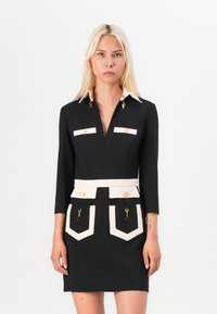 Black dress with three-quarter sleeves, white collar and pocket accents, gold hardware detailing, fitted silhouette, and textured fabric.