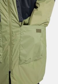 Light green waterproof jacket with a black inner lining, featuring a zipper, large side pocket, and textured fabric.