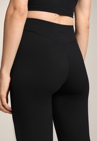 Fekete, magas derekú leggins, sima, rugalmas anyagból. A derékrészen varrási részlet található, és az alakhoz illeszkedő kialakítás jellemzi.