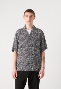 Short-sleeve button-up shirt in black and white with an abstract pattern. Features a camp collar and relaxed fit. Worn with black trousers.