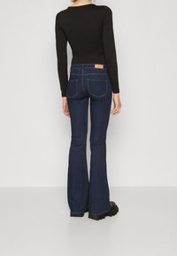 Uppvikta mörkblå jeans med sömnadsdetaljer, en läderetikett på baksidan, och en åtsittande svart långärmad topp i en slät textur.