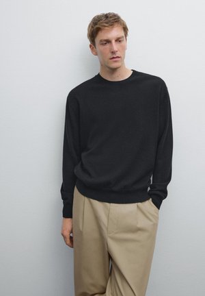 Black lightweight sweater with a round neckline and long sleeves, paired with beige trousers. Smooth fabric texture and relaxed fit.