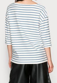 Vit randig topp med blå horisontella linjer, med trekvartsärmar och lös passform, tillverkad av mjukt, lätt tyg.