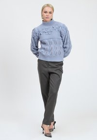 Hellblauer Strickpullover mit floralen Mustern, geripptem Kragen und Saum. Kombiniert mit dunkelgrauen Hosen und gemusterten High Heels.