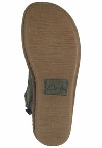 Suela de goma marrón con acabado texturado y logo de Clarks; forma curvada en la punta; tacón plano; se observan algunas señales de uso en la superficie.