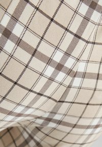 Béžová látka s hnědým a bílým kostkovaným vzorem. Materiál vypadá texturovaně s viditelnými tkanými detaily.