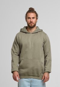 Sudadera verde oliva fabricada en un tejido suave, con un bolsillo frontal, capucha con cordón y puños acanalados. Diseño sencillo sin patrones.