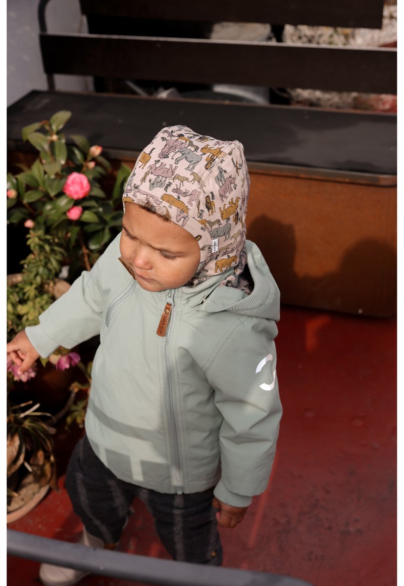 Veste à fermeture éclair vert clair avec capuche, dotée d'une fermeture éclair en bois marron. L'enfant porte une casquette à motifs beige avec des dessins d'animaux.