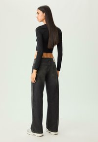 Top nero a maniche lunghe crop abbinato a jeans neri a gamba larga. I jeans presentano un design a due tasche e un logo discreto sulla vita.