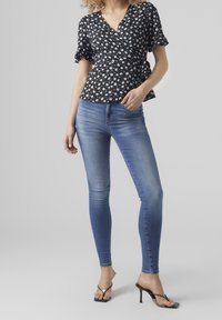 Top avvolgente nero a fiori con maniche corte, abbinato a jeans skinny blu a vita media e sandali neri con tacco. Tessuto liscio.
