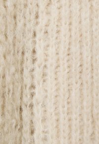 Stickad tyg i off-white med en mjuk, fluffig textur och distinkta vertikala ribbningar samt ojämna trådar för extra djup.