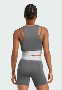 Gray athletic crop top with thin straps, featuring a white branded elastic band around the waist, paired with matching shorts.
