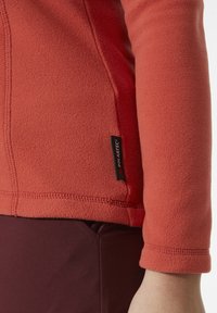 Rode fleecejack met een soepele textuur, voorzien van een gestikte zoom en een Polartec-label aan de linkerkant nabij de onderzoom.