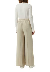 Beige wijde broek met een elastische tailleband en zijnaad. Gecombineerd met een fitted witte longsleeve top. Eenvoudige, gladde textuur.