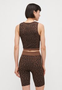 Hnedý crop top s leopardím vzorom a zodpovedajúce vysoké cyklistické šortky. Elastický materiál s rebrovanou textúrou a elastickým pásom.