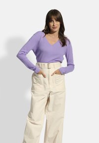 Lila v-hals sweater van zacht breimateriaal, gecombineerd met hoog-waisted crèmekleurige broek met een riem en zijzakken, die een ontspannen pasvorm laat zien.