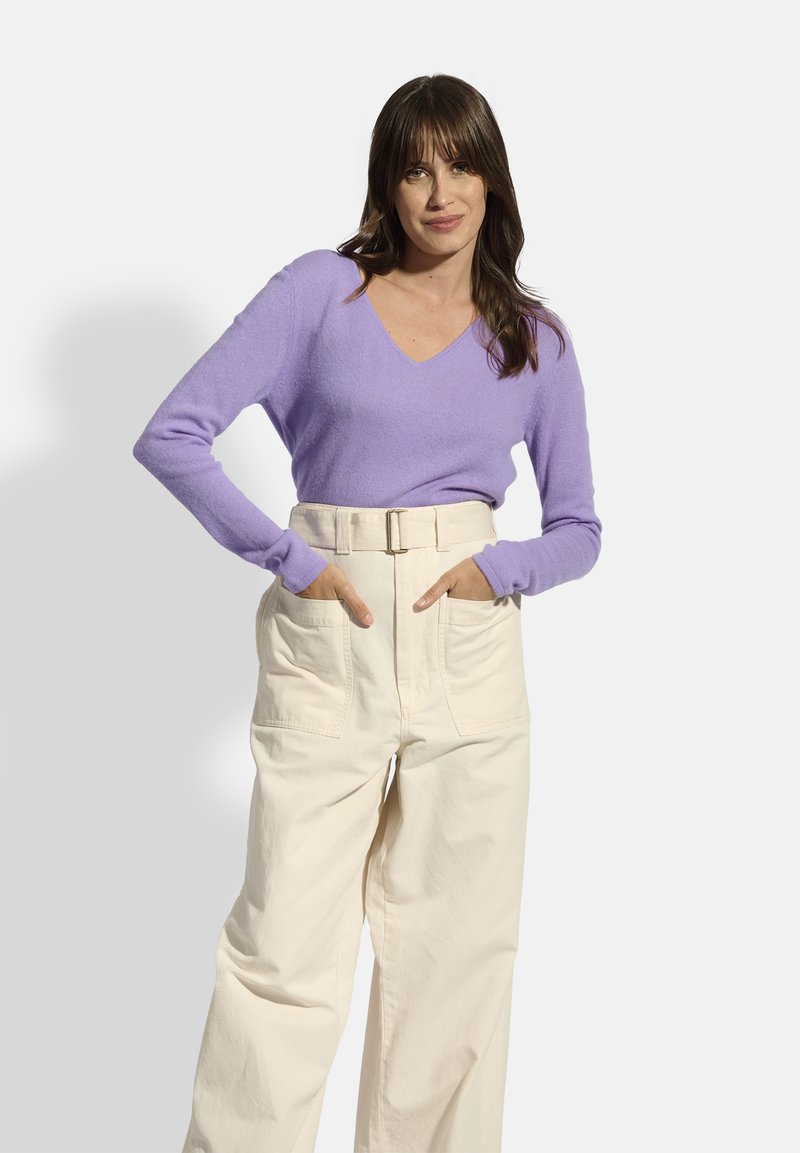 Lila v-hals sweater van zacht breimateriaal, gecombineerd met hoog-waisted crèmekleurige broek met een riem en zijzakken, die een ontspannen pasvorm laat zien.