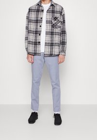 Svartvit rutig flanellskjorta med knappar fram och bröstficka, kombinerad med ljusblå slim fit-byxor och svarta skor.