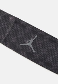 Faixa atlética preta com um padrão de malha texturizada, apresentando um logo Jumpman refletor em cinza de um lado.