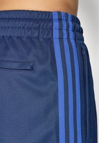 Calças de desporto azul marinho com um tecido texturizado, cintura elástica e três riscas verticais em azul escuro e azul claro de cada lado.