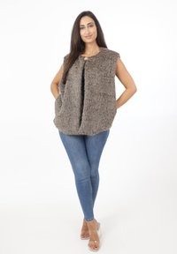 Faux fur-väst i gråbrunt, ärmlös design med framfickor, öppen framsida, strukturerad yta, i kombination med blå skinny jeans och genomskinliga klackar.