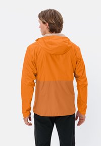Oranje waterdichte jas met een capuchon en een contrasterend lichter oranje paneel op de taille. Heeft een gladde textuur en een getailleerd ontwerp.