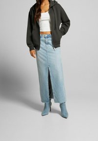 Felpa nera con zip, top corto bianco, gonna maxi in denim azzurro chiaro con spacco frontale, abbinata a stivaletti azzurro chiaro.