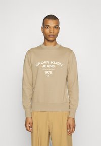 Felpa beige con collo a giro e stampa "CALVIN KLEIN JEANS 1978". Tessuto morbido, polsini e orlo a costine, design minimalista.