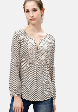 Blusa de manga larga con escote en V, hecha de una tela ligera con un patrón geométrico en blanco y negro y detalles fruncidos en la cintura.